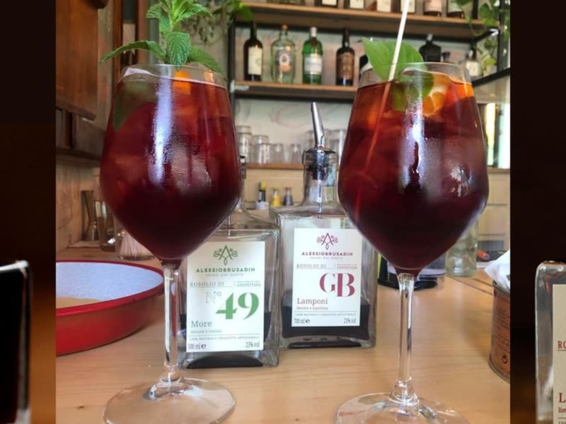 Two glasses of rosolio spritz between the bottles of Rosolio n°49 and GB