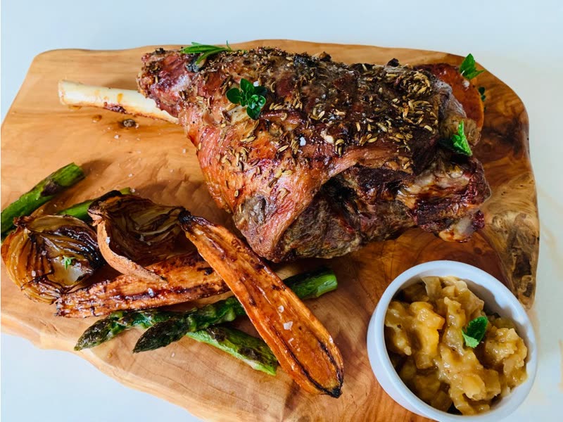 Roast leg of lamb with oven-baked vegetables and a bowl of chutney